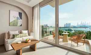 Interiør av stue med sofa og bord, samt utsikt over balkong og bysilhuett. (AI-generert tekst)