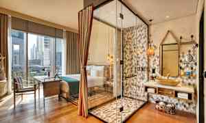 Et hotellrom med store vinduer. Et dusjområde med glassvegger er synlig ved siden av en servant og speil. (AI-generert tekst)