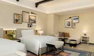 Et hotellrom med to senger, sofa og dekorative malerier på veggen. (AI-generert tekst)