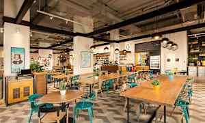 Interiør av en moderne restaurant med trebord, fargerike stoler og dekorative planter. (AI-generert tekst)