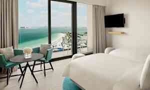 Hotellrom med to senger, bord og stoler samt utsikt mot en strand og havet. (AI-generert tekst)