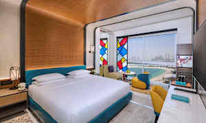 Et hotellrom med en stor seng, fargerike glassmalerier og utsikt over stranden og byen. (AI-generert tekst)