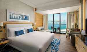 Hotellrom med dobbeltseng, sittegruppe og balkong med utsikt over havet. (AI-generert tekst)