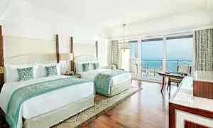 Hotellrom med to store senger, lys innredning og havutsikt fra en balkong. (AI-generert tekst)