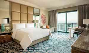 Et luksuriøst hotellrom med dobbeltseng, sittegruppe og havutsikt. (AI-generert tekst)