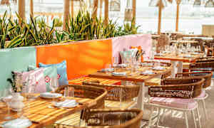 En uteservering med dekkede bord, fargerike puter og grøntområder. (AI-generert tekst)