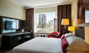 Bilde av et moderne hotellrom med en seng i forgrunnen, et skrivebord med en TV og et vindu med utsikt over en by. (AI-generert tekst)