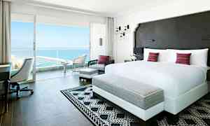 Lyst og moderne hotellrom med en stor dobbeltseng og utgang til balkong med havutsikt. (AI-generert tekst)