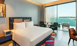 Et moderne hotellrom med en stor seng, sitteplasser og et stort vindu med utsikt over havet. (AI-generert tekst)