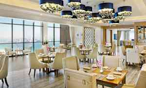 Interiør av en elegant restaurant med havutsikt, lyse møbler og dekorative lysekroner. (AI-generert tekst)