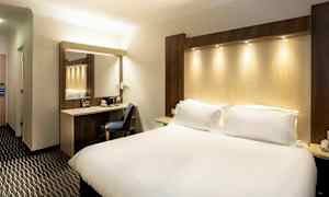 Et hotellrom med en stor seng, en arbeidsplass med stol og et speil. (AI-generert tekst)