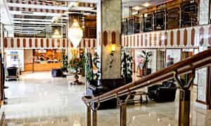 En hotellobby med marmorgulv, en resepsjonsdisk i bakgrunnen og sitteplasser. (AI-generert tekst)