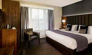 Et hotellrom med stor seng, lenestol og treinnredede detaljer. (AI-generert tekst)