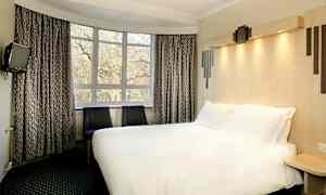 Et hotellrom med en stor seng, to stoler og et vindu med utsikt mot trær. (AI-generert tekst)