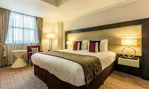 Et hotellrom med en stor seng, dekorative puter, lamper og møbler. (AI-generert tekst)