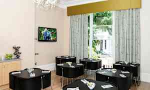 Et lyst rom med flere mørke bord og stoler samt en stor vindu mot grøntområde. (AI-generert tekst)