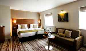 Hotellrom med to enkeltsenger og en sofa. (AI-generert tekst)