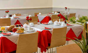 Et rom med dekkede bord, røde og hvite duker, og tallerkener med frokostmat. (AI-generert tekst)