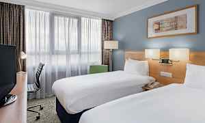 Hotellrom med to enkeltsenger, skrivebord og stol. (AI-generert tekst)