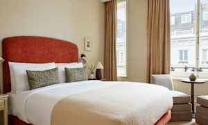 Soverom med stor seng, to dekorative puter, lamper ved sidene, og vindu med gardiner. (AI-generert tekst)