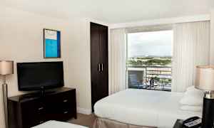 Et hotellrom med to senger, en TV på en kommode, et skap og en balkong med utsikt. (AI-generert tekst)