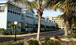 En rekke blå bygninger med hvite vinduer, omkranset av palmer og en steinete hage. (AI-generert tekst)