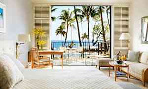 Hotellrom med lys innredning, en seng, en sittegruppe og en balkong med utsikt over havet og palmetrær. (AI-generert tekst)