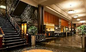 Bilde av hotellets lobby med marmorgulv, en trapp, sofaer og plantearrangement. (AI-generert tekst)