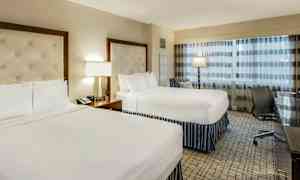 Et hotellrom med to dobbeltsenger, en lampe og et skrivebord ved siden av en stol. (AI-generert tekst)