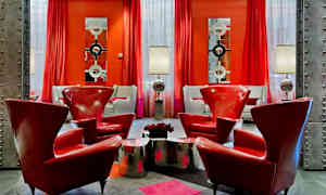 Et stilfullt innredet rom med røde lenestoler, metalliske bord og lamper samt røde gardiner og moderne speil på veggene. (AI-generert tekst)