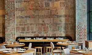 Et rom med murvegger og trebord, arrangert for restaurantbruk. (AI-generert tekst)