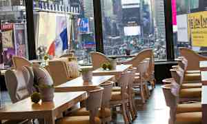 Restaurant med trebord og stoler, med utsikt over byens neonlys og storskjermer. (AI-generert tekst)