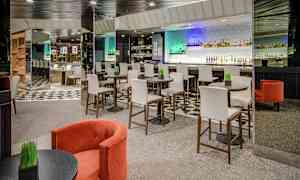 Interiør av en moderne bar med høye stoler ved runde bord og en bardisk i bakgrunnen. (AI-generert tekst)