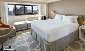 Et hotellrom med en stor seng og utsikt mot byen gjennom vinduet. (AI-generert tekst)