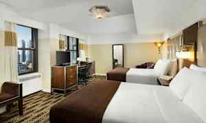 Et hotellrom med to dobbeltsenger, skrivebord, TV og to store vinduer. (AI-generert tekst)