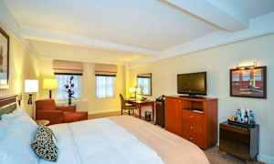 Et hotellrom med en stor seng, en lenestol, et skrivebord og en TV på en kommode. (AI-generert tekst)