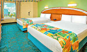 Et hotellrom med to enkeltsenger dekket med fargerike sengetepper. Veggene er malt i grønt, og det er et vindu med utsikt over en stjerneformet konstruksjon. (AI-generert tekst)