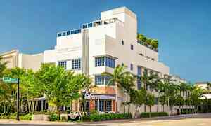 En hvit bygning i moderne stil med blå vindusrammer, omgitt av trær og palmer. (AI-generert tekst)