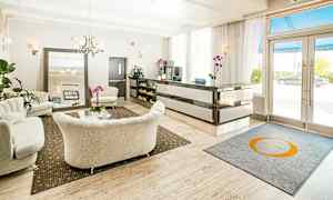 En hotellobby med lyse sofaer, et resepsjonsområde og et bord dekorert med orkideer. (AI-generert tekst)