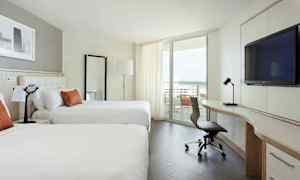 Et moderne hotellrom med to store senger, et skrivebord med en stol, og en balkong med utsikt over havet. (AI-generert tekst)