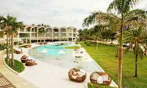 Et utendørs basseng ved et moderne hotell omgitt av palmer og grøntområder. Solsenger og skyggefulle parasoller er plassert ved bassenget. (AI-generert tekst)