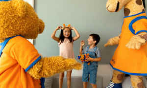 To barn interagerer med en bjørne- og sjiraffmaskot og ser ut til å ha det gøy. (AI-generert tekst)