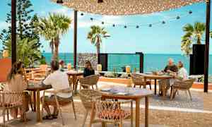 Uteservering med bord og stoler foran havutsikten. (AI-generert tekst)