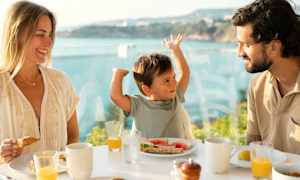 En familie spiser frokost ved et bord med utsikt over havet. (AI-generert tekst)