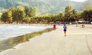 Sandstrand med mennesker, palmer og fjell i bakgrunnen. (AI-generert tekst)