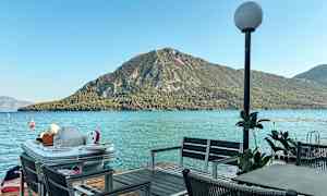 Et bord med stoler ved en brygge med utsikt over havet og en grønnkledd fjellknaus. (AI-generert tekst)