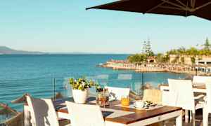 Utsikt over havet fra en restaurantterrasse med hvite bord og stoler. (AI-generert tekst)