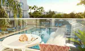 Utsikt fra en terrasse som viser et basseng med solsenger og parasoller omgitt av grøntområder. (AI-generert tekst)