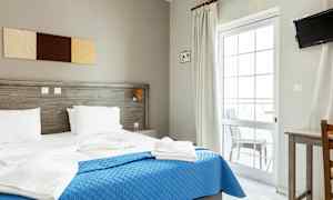 Et hotellrom med en dobbeltseng, blått sengeteppe og hvitt sengetøy. (AI-generert tekst)