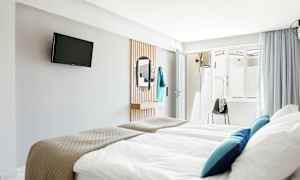 Hotellrom med senger, TV på veggen og et speil. (AI-generert tekst)